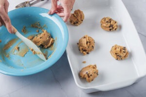 Scooping vegan chocolate chip cookie dough onto a baking sheet