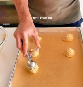 Scooping 3 ingredient pineapple cookie dough onto a baking sheet before baking
