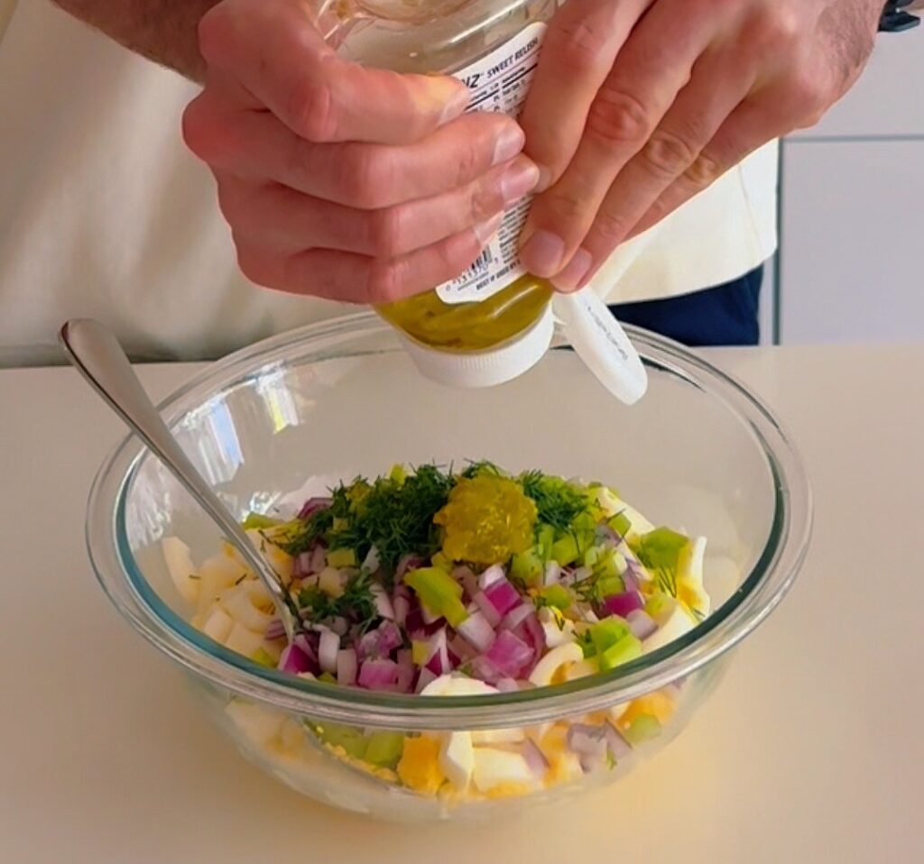 Adding dressing to a bowl of egg salad ingredients