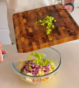 Chopped red onion and herbs being added to a bowl for high protein egg salad