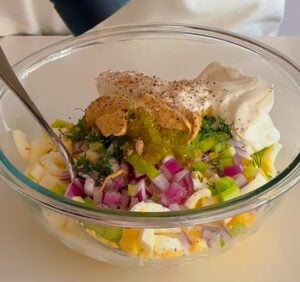 Egg salad ingredients in a glass bowl with yogurt and seasonings
