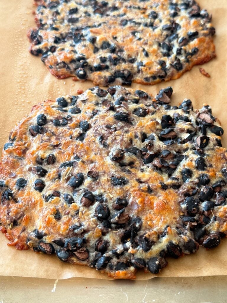 Two bean wraps browning in the oven on a professional sheet tray with parchment paper.