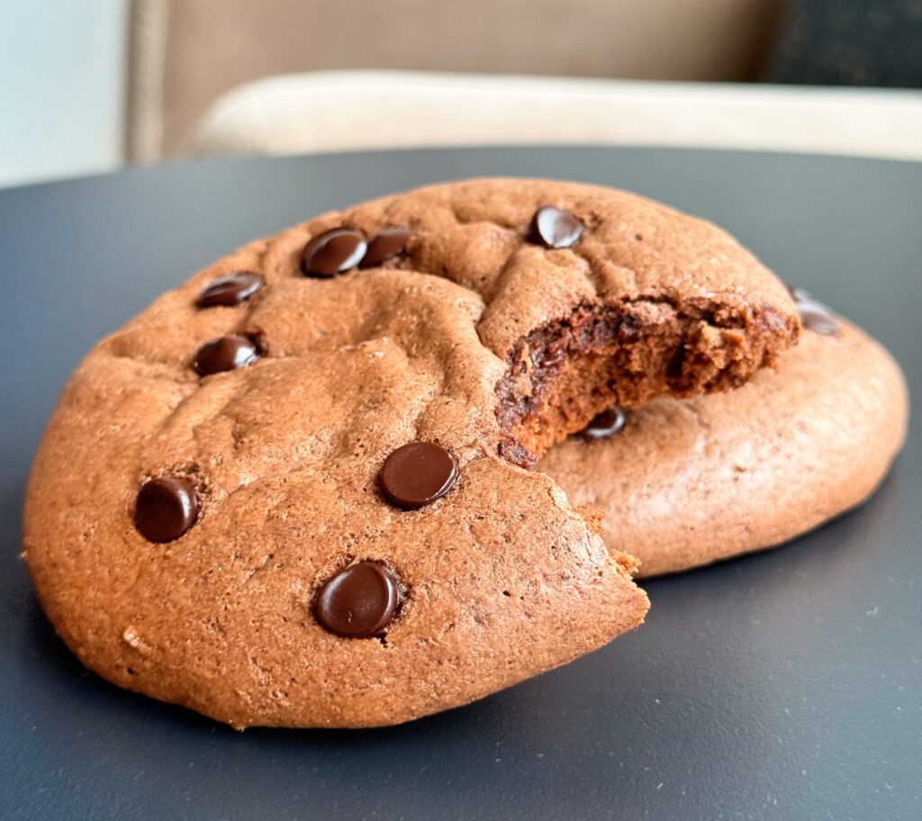 A high protein brownie cookie with a bite taken out, revealing a dense, fudgy, chocolatey center.