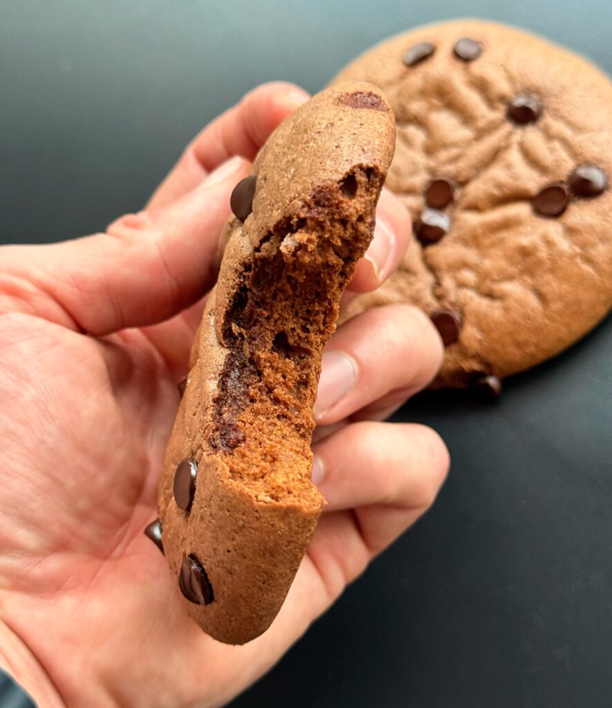 Freshly baked high protein brownie cookies with chocolate chips on a parchment-lined baking sheet.