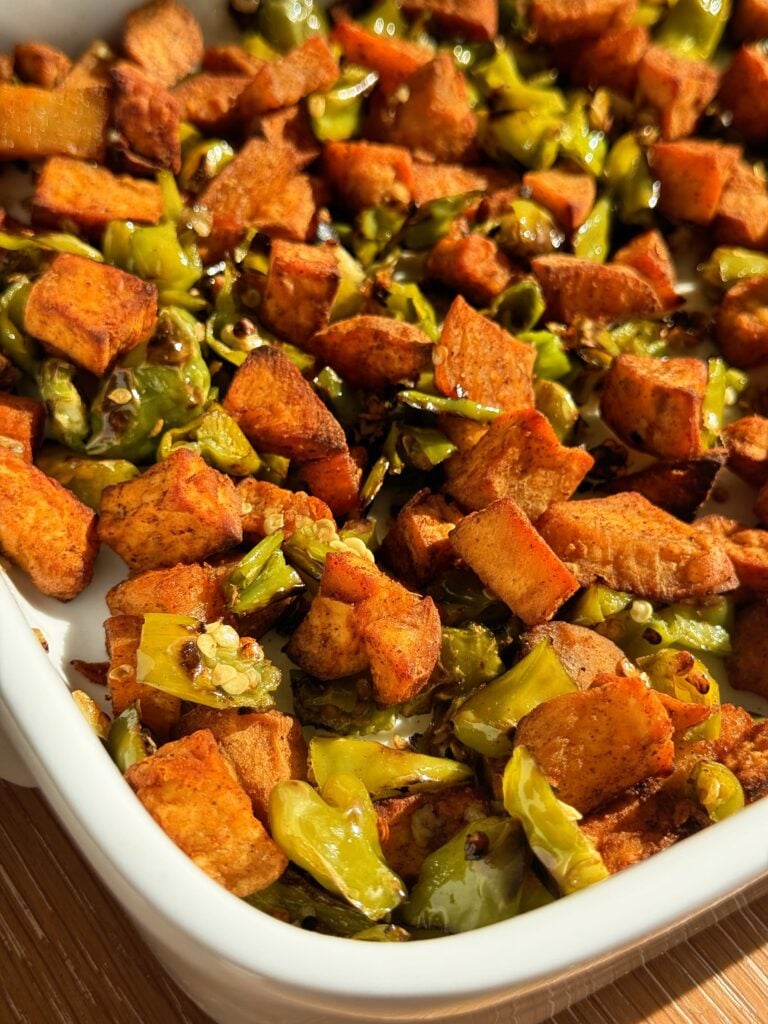 A colorful, high-volume breakfast hash with roasted sweet potatoes, charred shishito peppers, and caramelized onions in a cast-iron skillet.