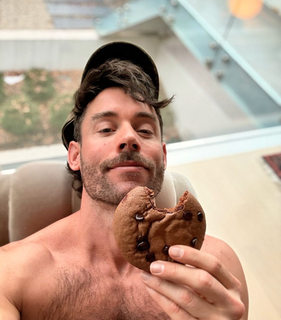A large, thick high protein brownie cookie being held to show the scale and soft texture.