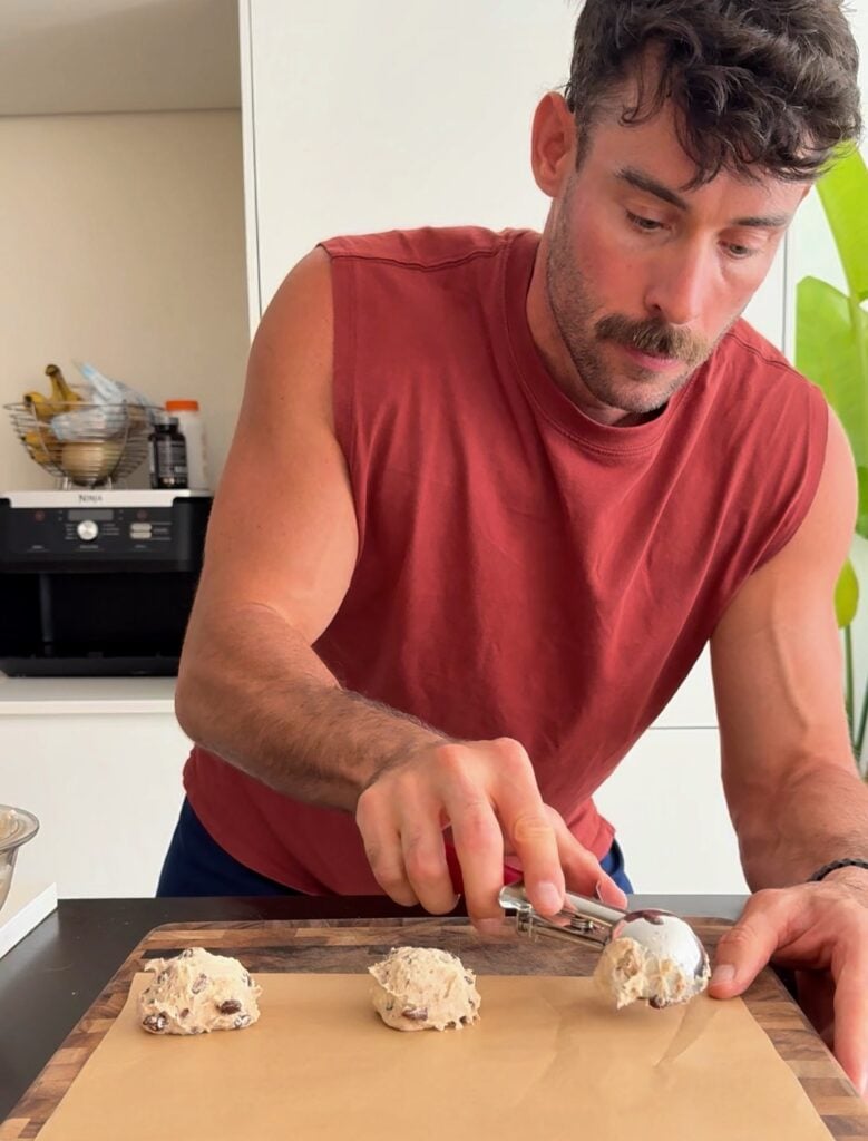 Hands rolling small portions of 2-ingredient protein bagel dough into uniform balls on a floured surface.