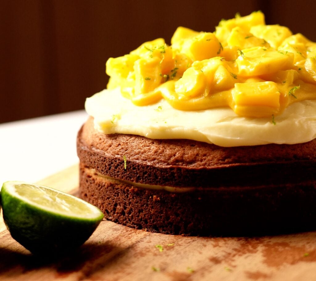 Fully assembled layer cake topped with cream cheese frosting and fresh diced mango cubes.