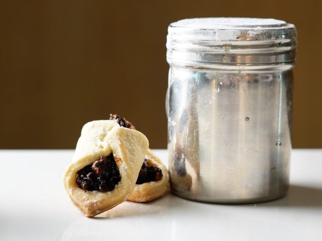 lekvar filled cookies being dusted with powdered sugar on counter