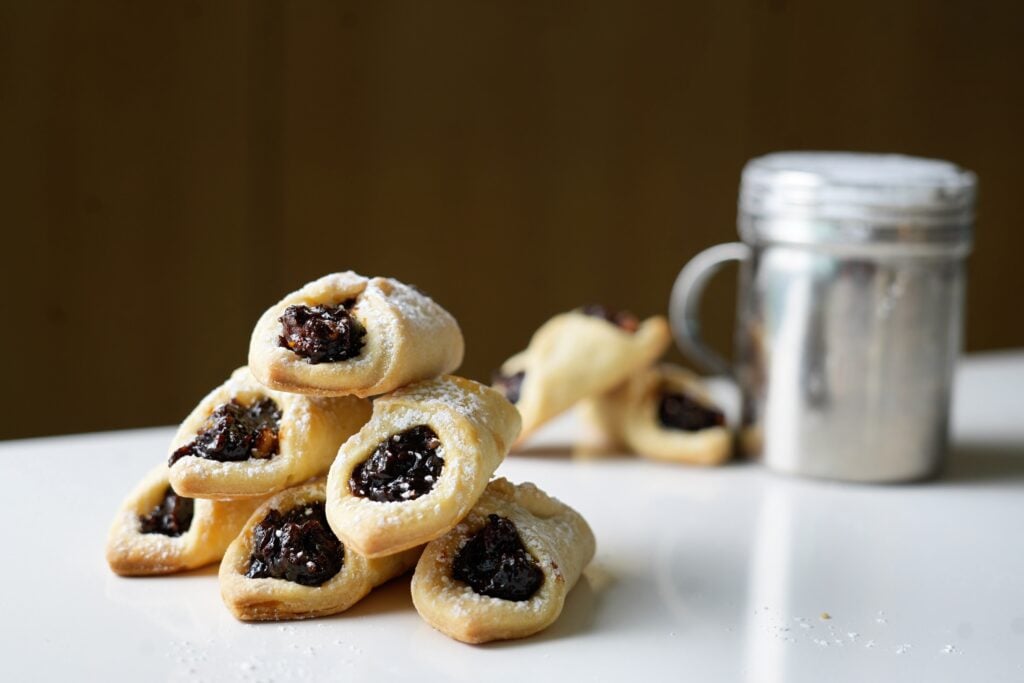lekvar filled cookies being dusted with powdered sugar on counter wide shot
