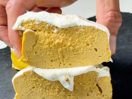 Hand holding two stacked slices of high protein pumpkin pie cheesecake