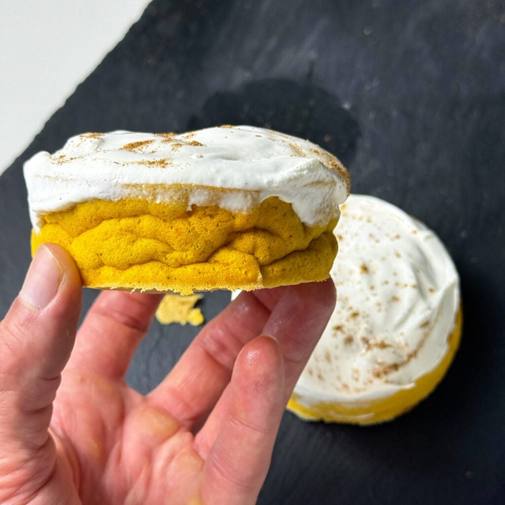 Hand holding a slice of high protein pumpkin pie cheesecake over a plate