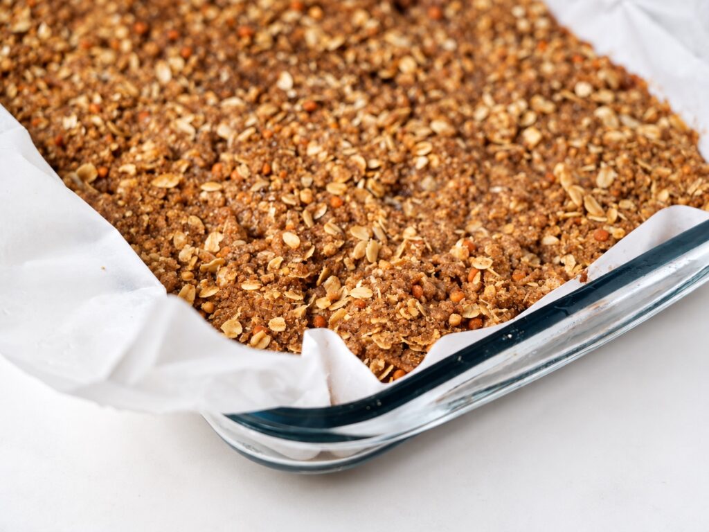Close-up of assembled gluten-free apple pie bars covered with oat streusel in a parchment-lined pan.