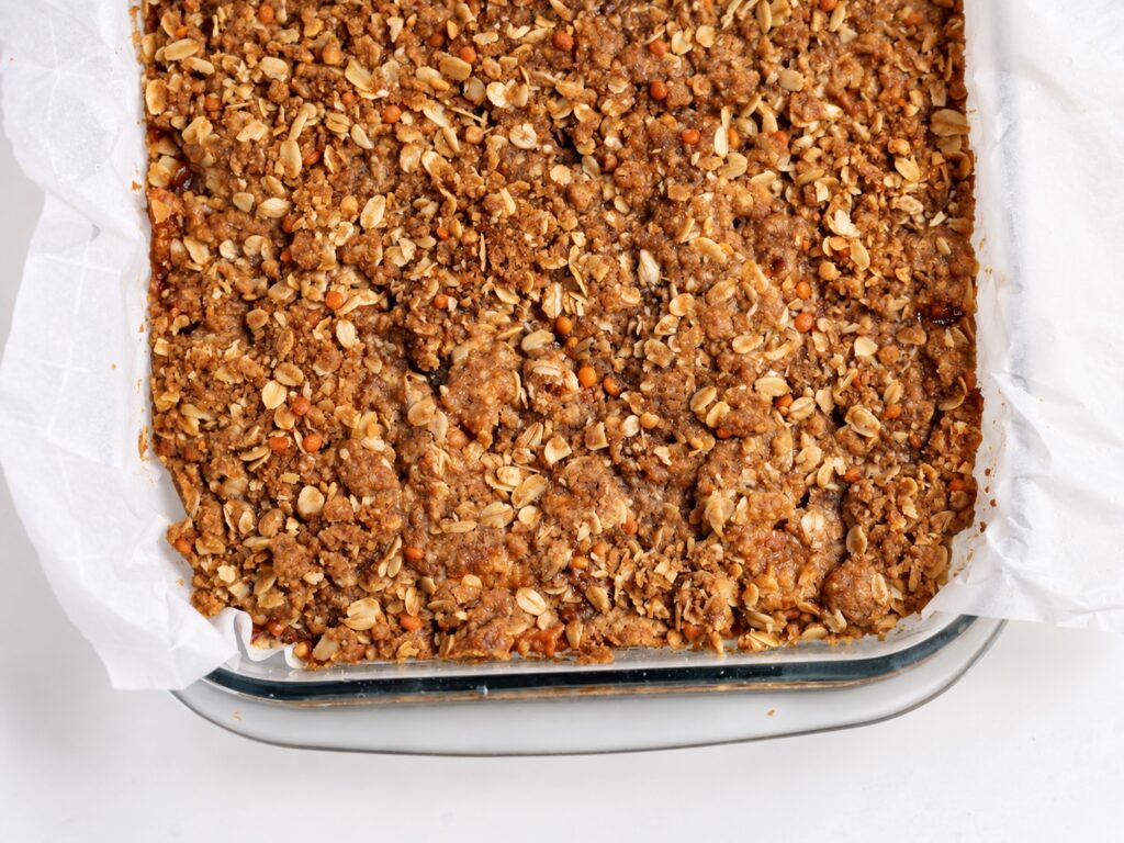 Overhead view of baked gluten-free apple pie bars with oat streusel in a parchment-lined square pan.