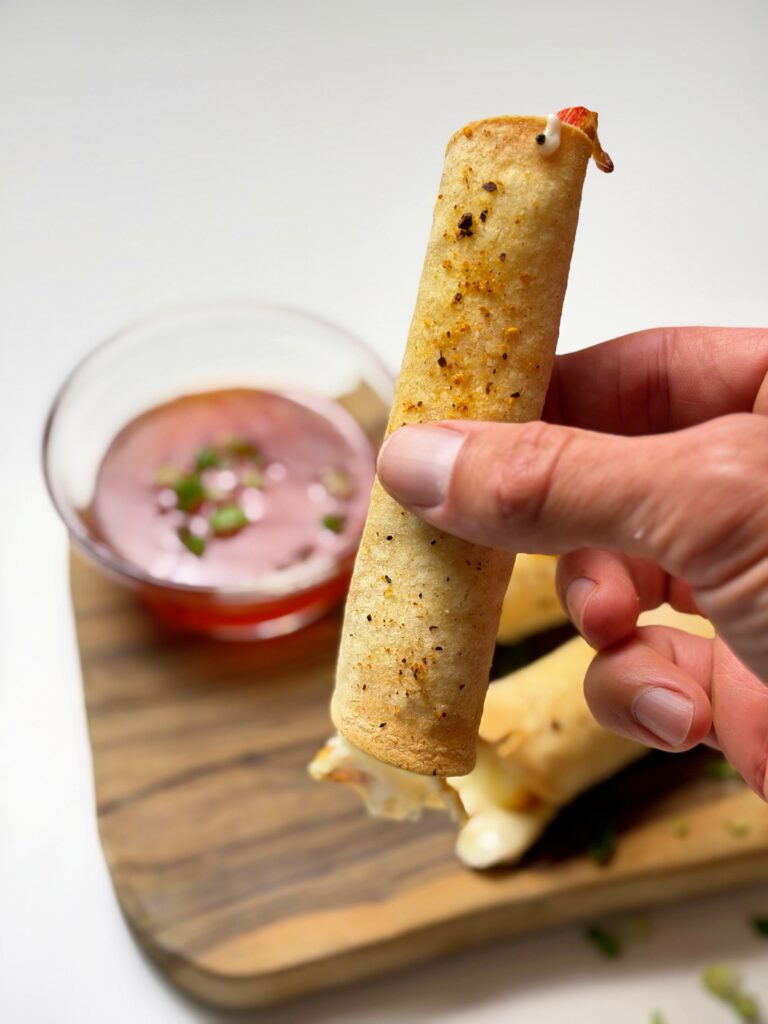 Hand holding a crispy crab rangoon mozzarella taquito above a wooden serving board.
