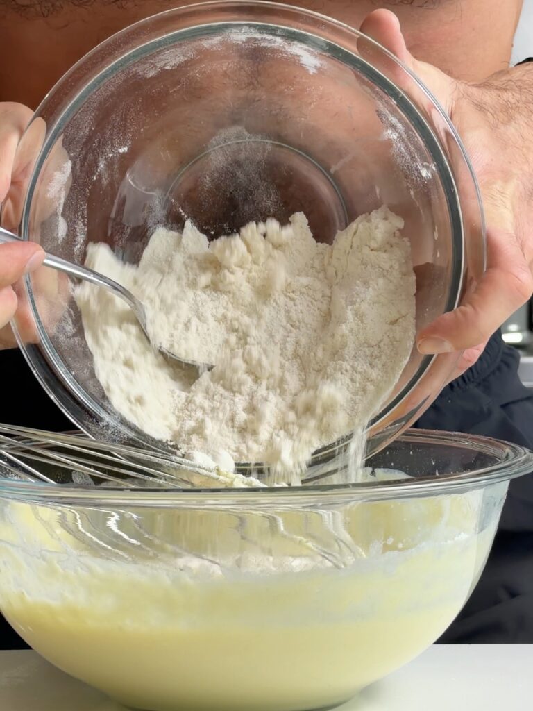 Jacob adding the dry cake mix and protein powder mixture to the wet ingredients in a glass bowl.