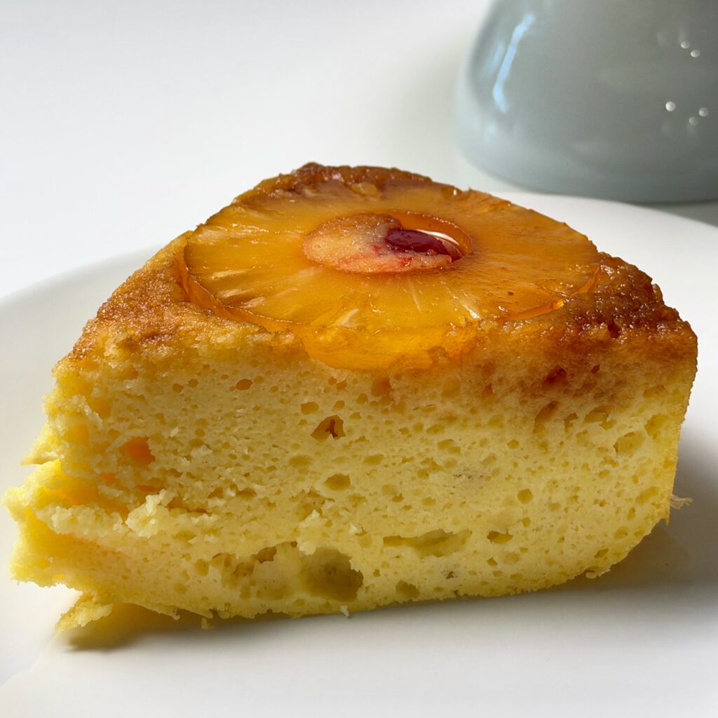 Close-up of a thick slice of pineapple upside-down protein cake topped with a pineapple ring and cherry.