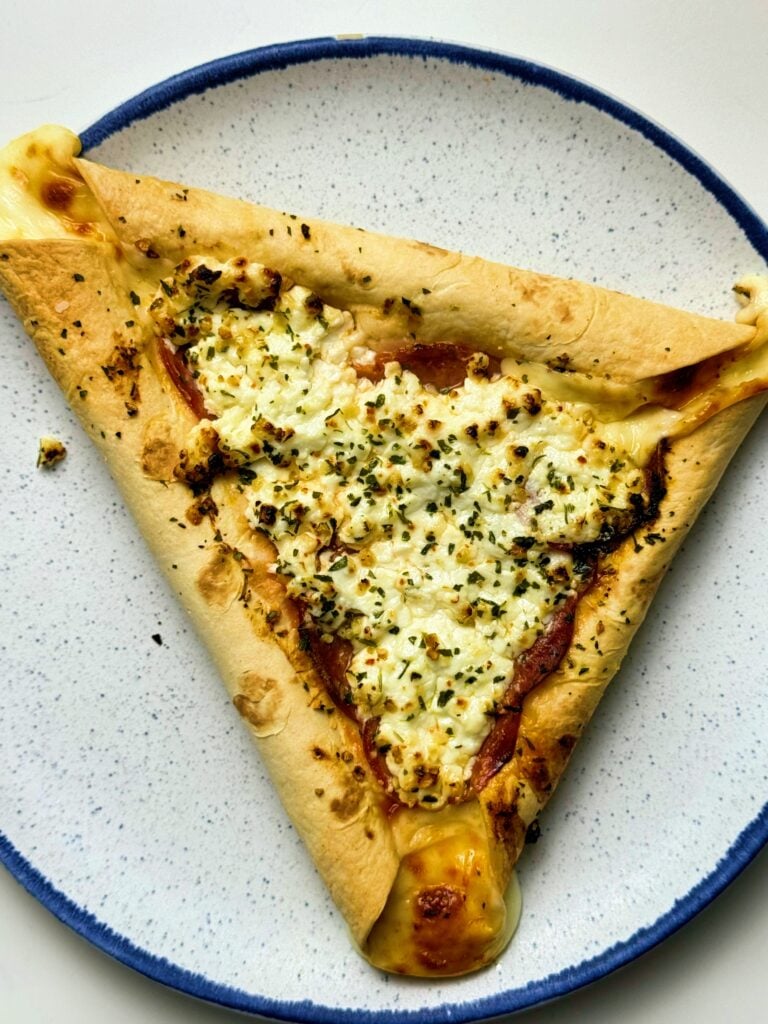 Triangular low-calorie stuffed crust personal pizza with cottage cheese, pepperoni, and herbs on a blue-rimmed plate.