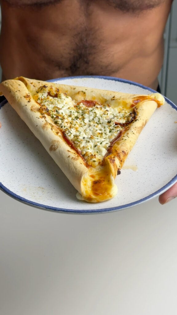 Jacob Hensley holding a plate with a triangular stuffed crust tortilla pizza topped with cottage cheese, pepperoni, and herbs.