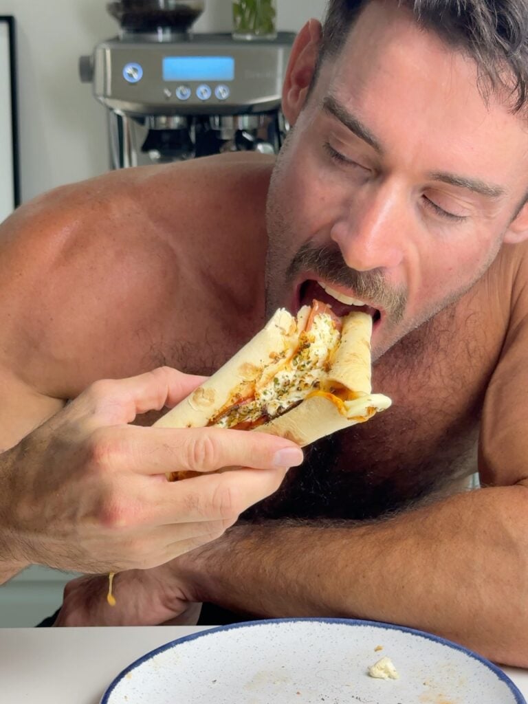 Close-up of Jacob Hensley biting into a stuffed crust tortilla pizza with cottage cheese and pepperoni.