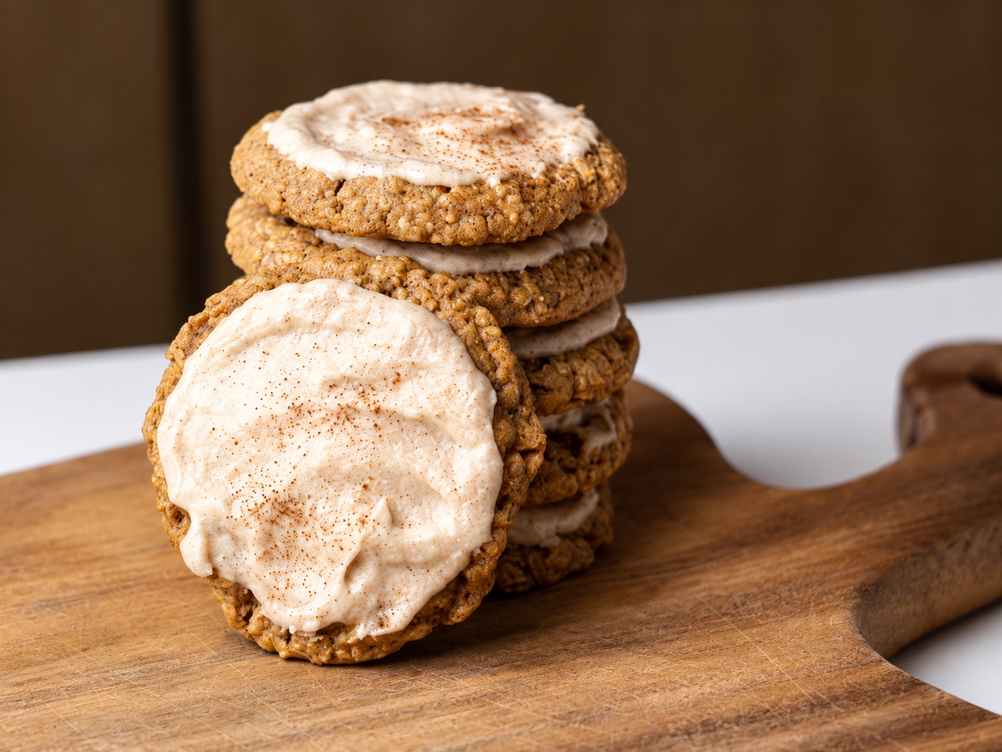 Stack of apple butter oatmeal cookies with cinnamon frosting on a wooden serving board.