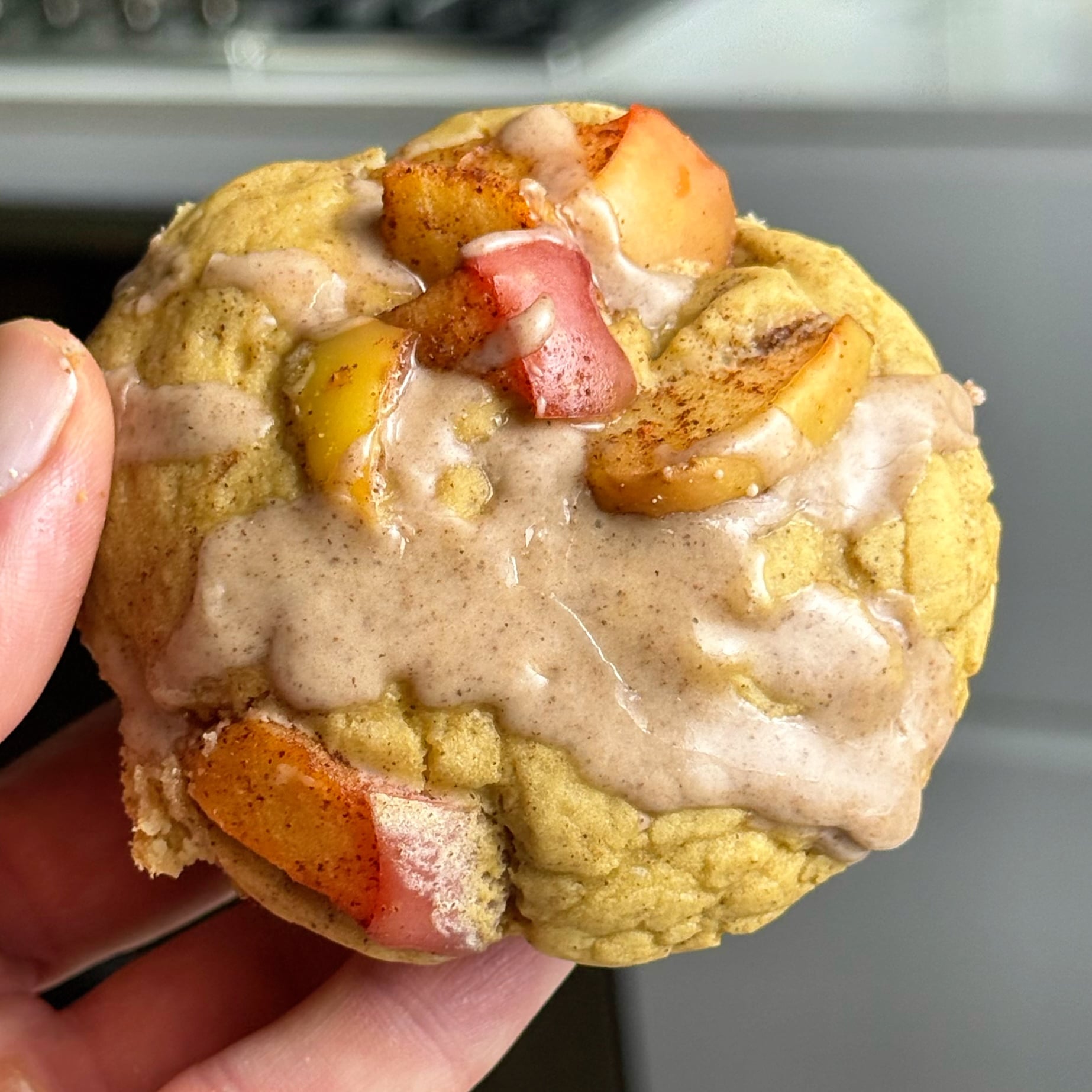 Hand holding an apple pie protein muffin with diced apples and cinnamon glaze on top.