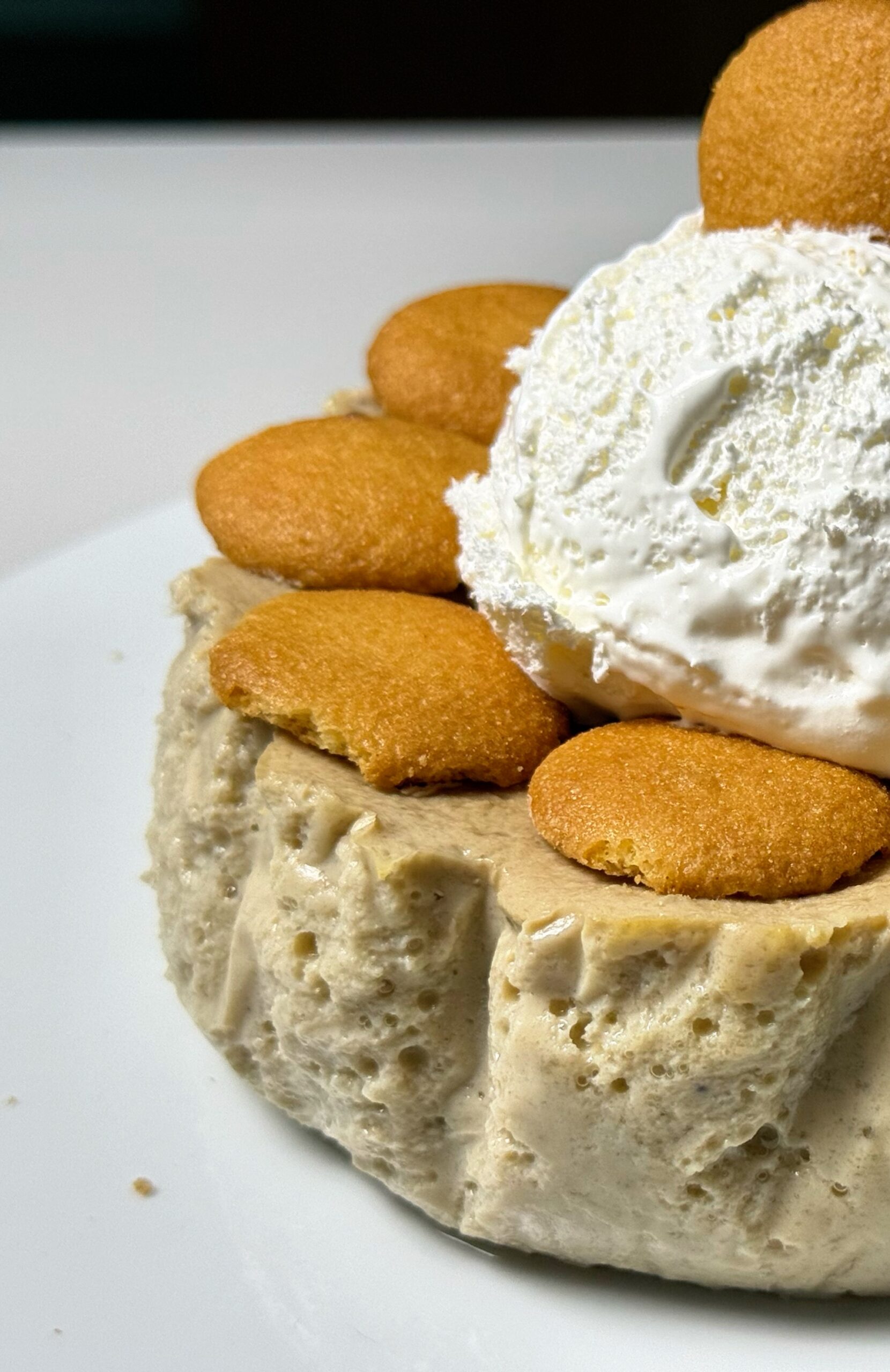 Close-up of whipped cream and vanilla wafer cookies on top of banana cream cheesecake.