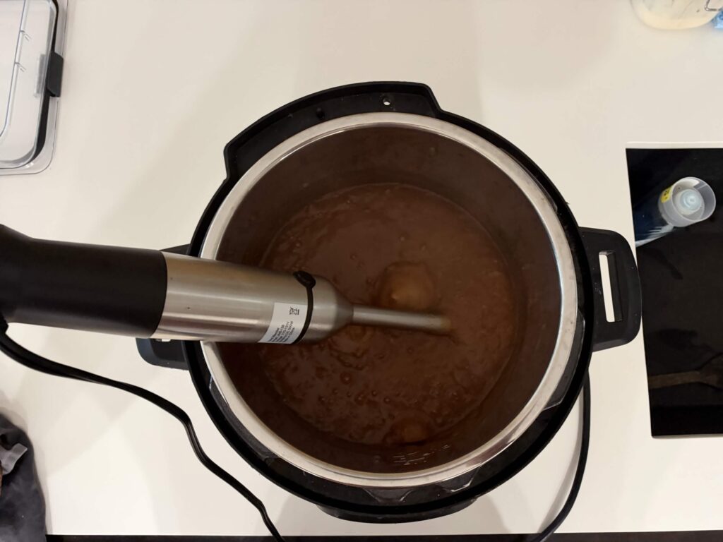Cooked apples being puréed until smooth with an immersion blender.