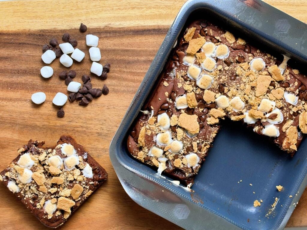 Chocolate banana s'mores brownies in the baking pan beside a cut square with chocolate chips and mini marshmallows