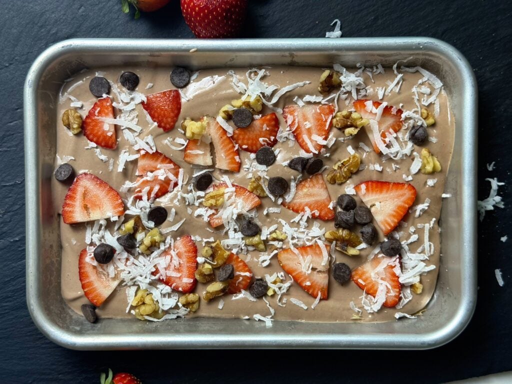 Overhead view of chocolate Greek yogurt bark with strawberries, walnuts, coconut, and chocolate chips in a small sheet pan