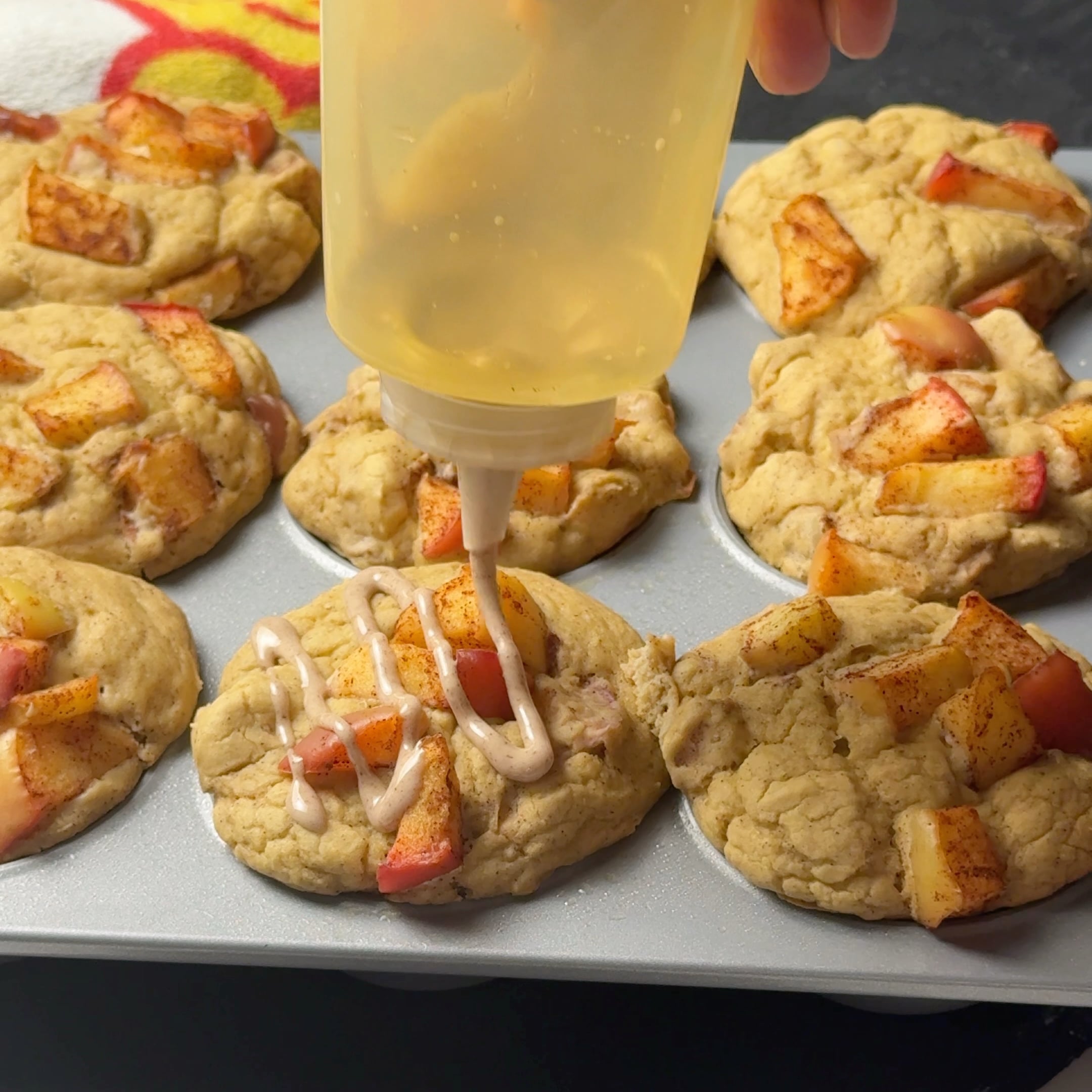 Spoon drizzling cinnamon glaze over baked apple pie protein muffins.