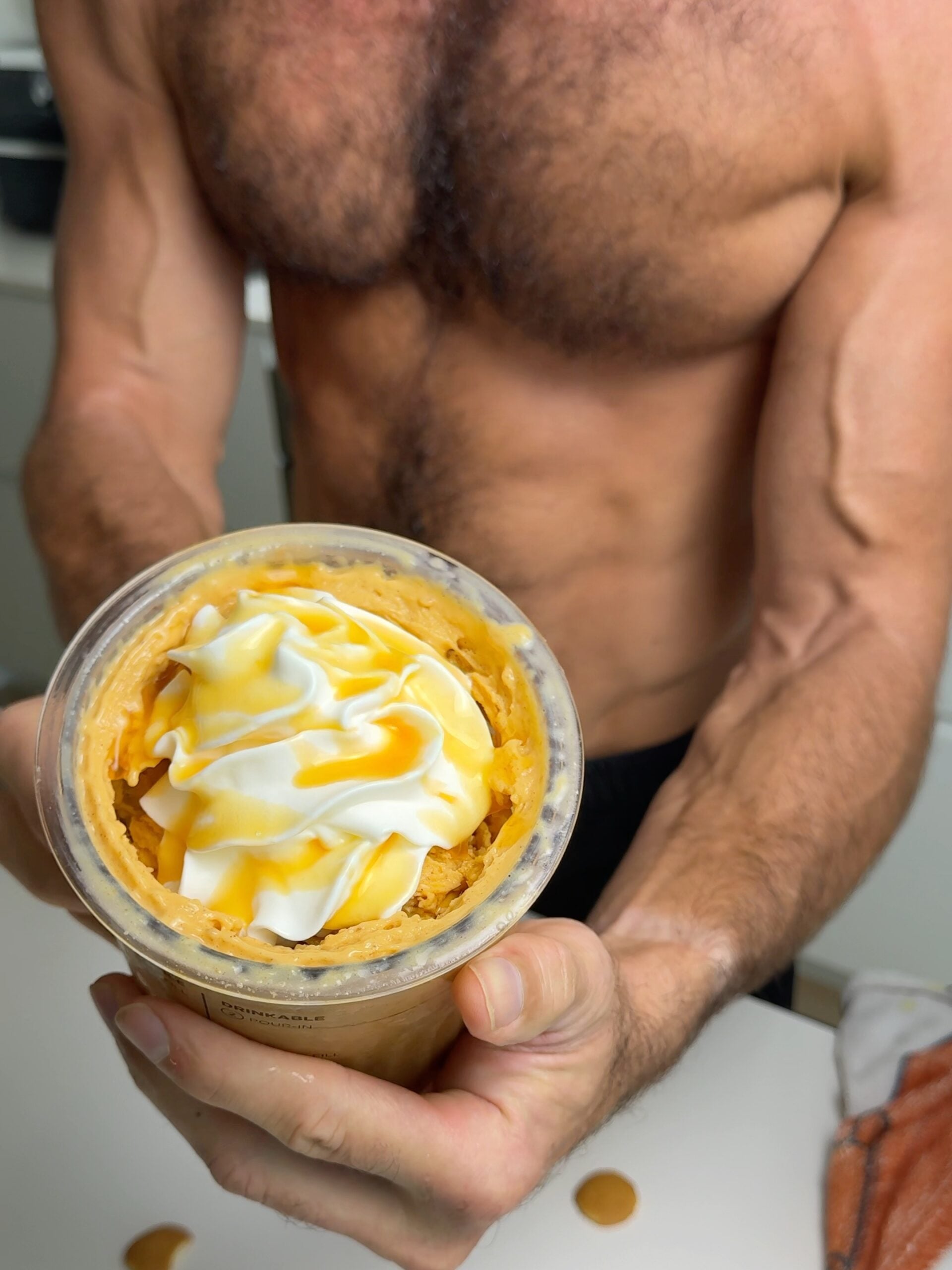 Person holding a pint of high-protein pumpkin pie Ninja Creami topped with whipped cream and syrup