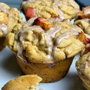 Close-up of apple pie protein muffins topped with diced apples, cinnamon crumble, and glaze.