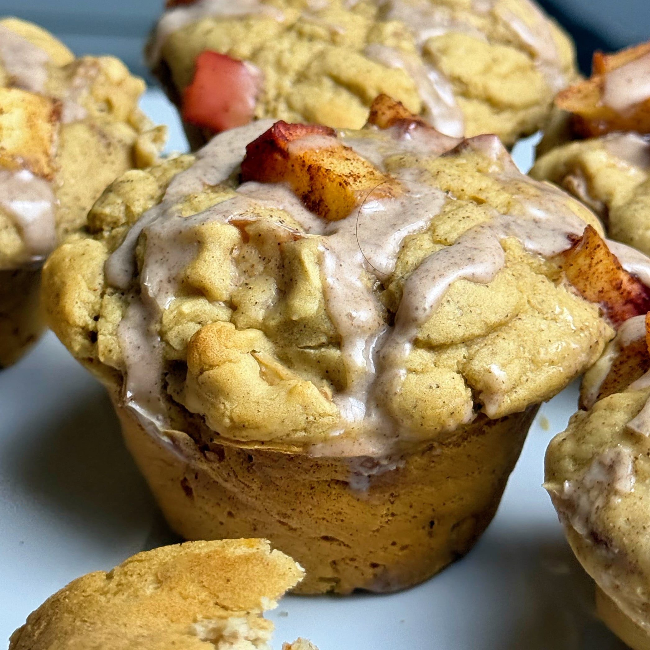 Close-up of apple pie protein muffins topped with diced apples, cinnamon crumble, and glaze.