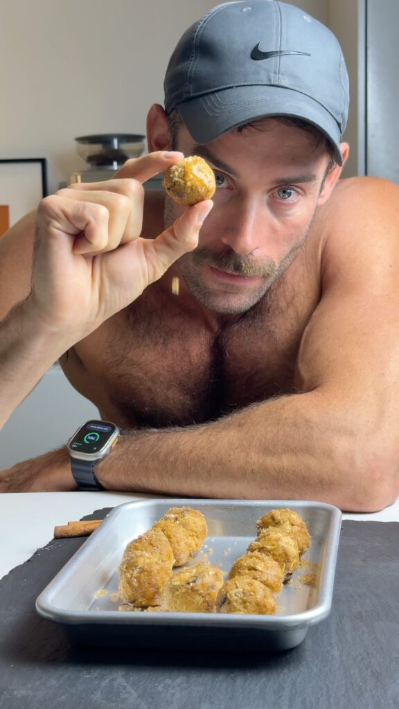 Jacob holding a pumpkin spice protein ball near his face, with a tray of finished balls on the counter.