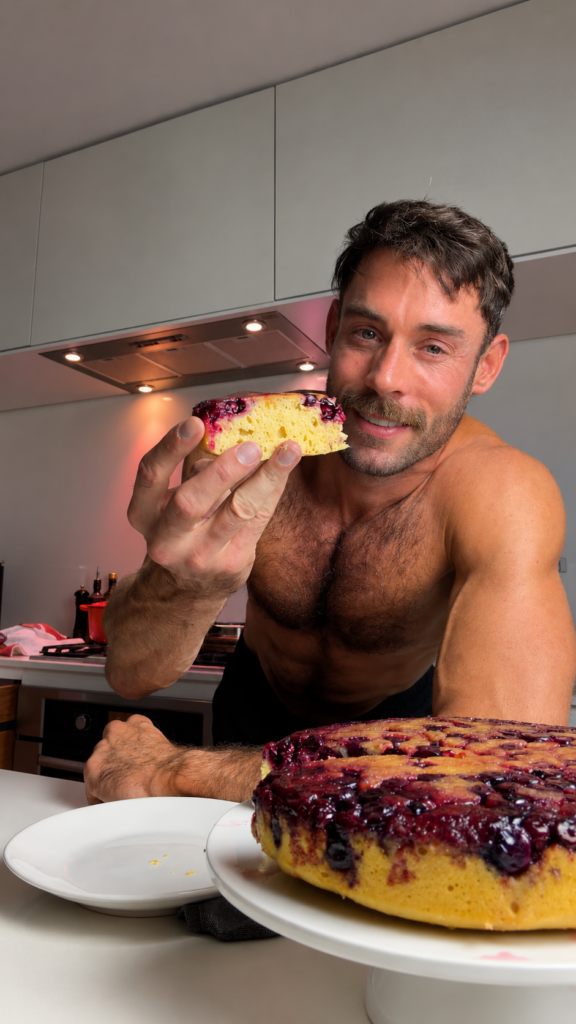 Jacob holding a slice of lemon blueberry upside-down cake beside the finished cake in his kitchen.