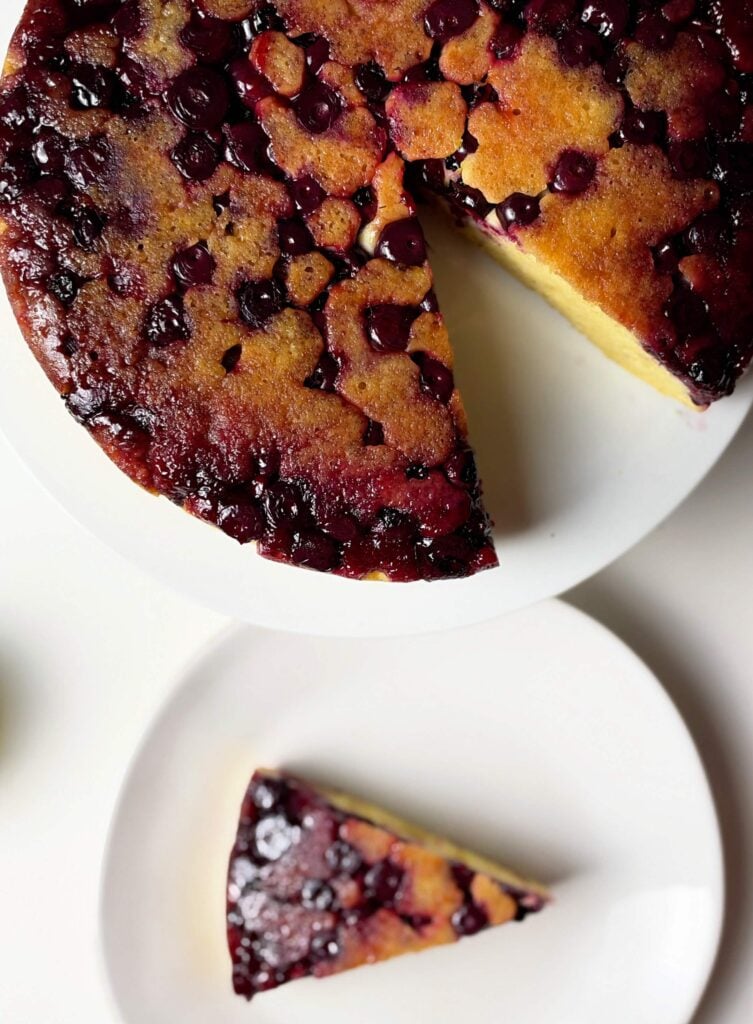 Lemon blueberry upside-down cake with one slice removed and served on a white plate.