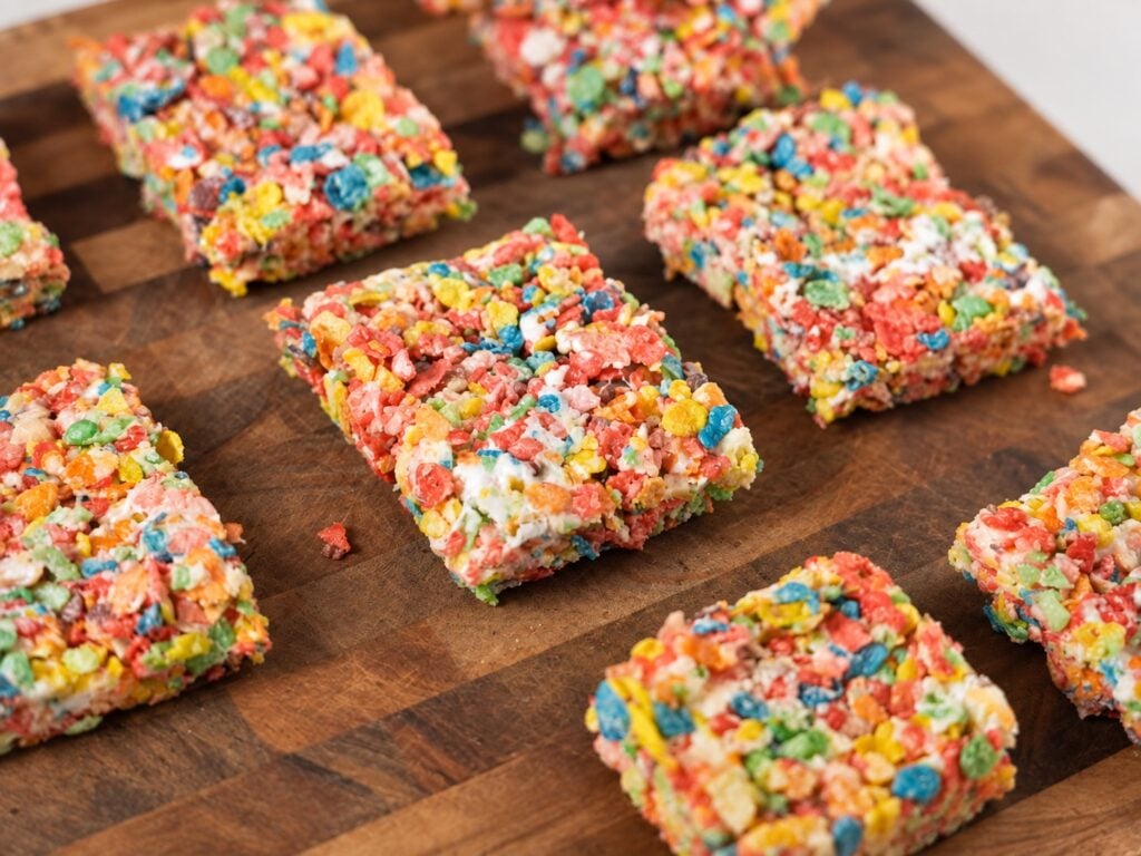 Close-up of protein Fruity Pebbles rice crispy treats spread across a wooden cutting board.