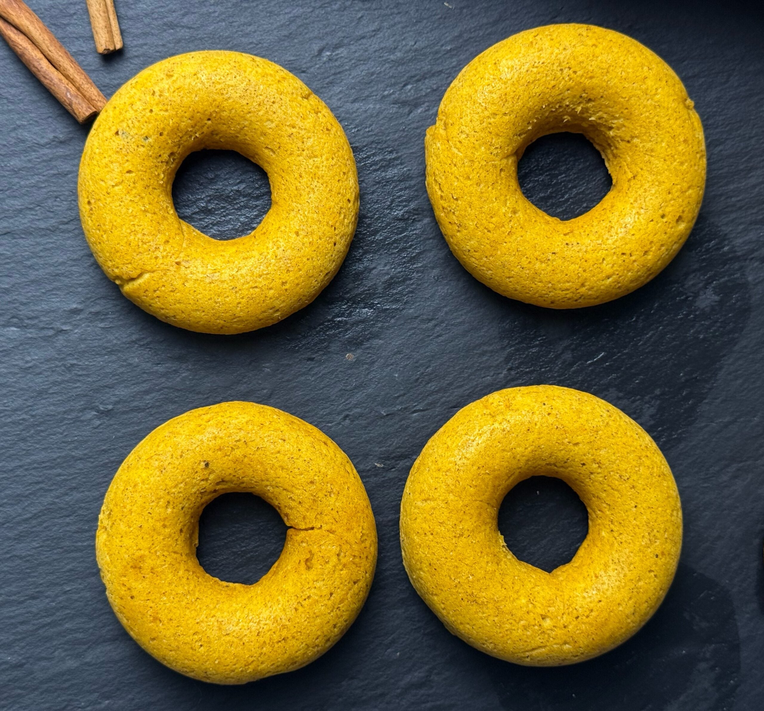 Baked pumpkin spice donuts on a dark slate board with cinnamon sticks