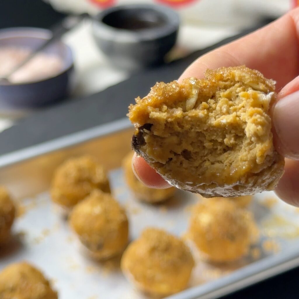 Close-up of a bitten pumpkin spice protein ball held above a tray, showing oats and a chocolate chip inside.