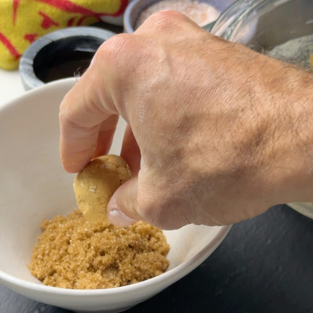 Hand rolling a pumpkin spice protein ball in brown sugar in a white bowl.
