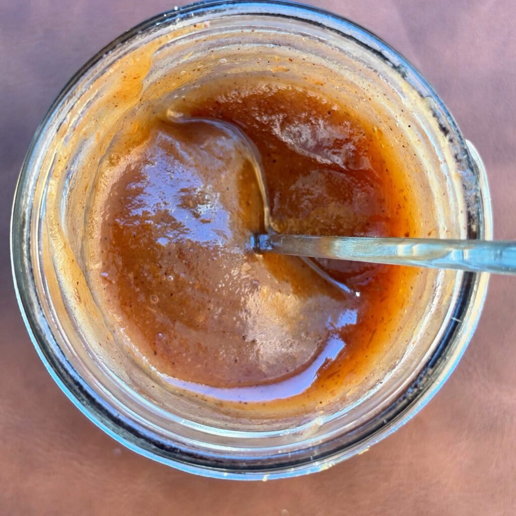 Close overhead view of smooth homemade apple butter in a glass jar with a spoon.