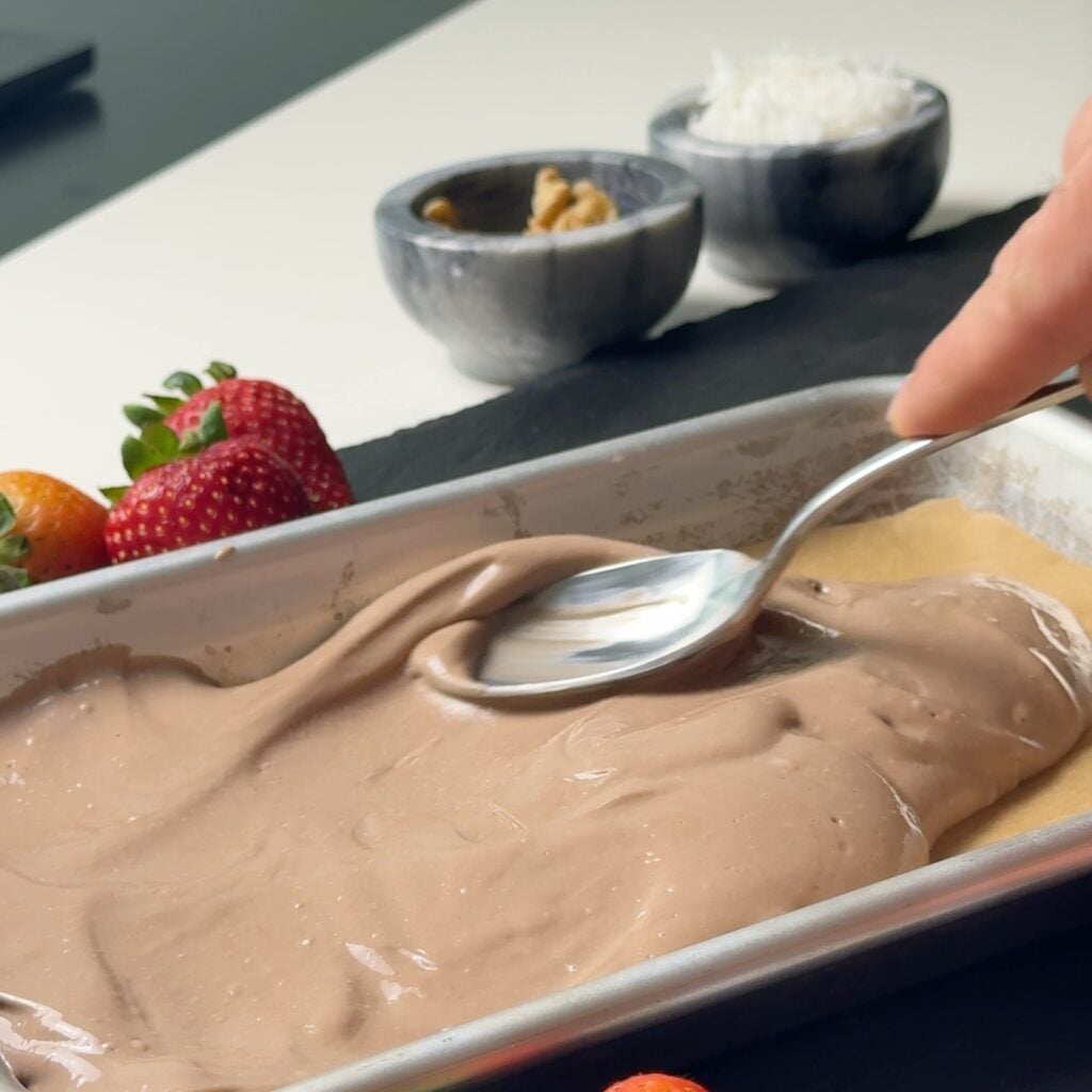 Chocolate Greek yogurt and protein powder mixture being spread evenly in an eighth-sheet pan