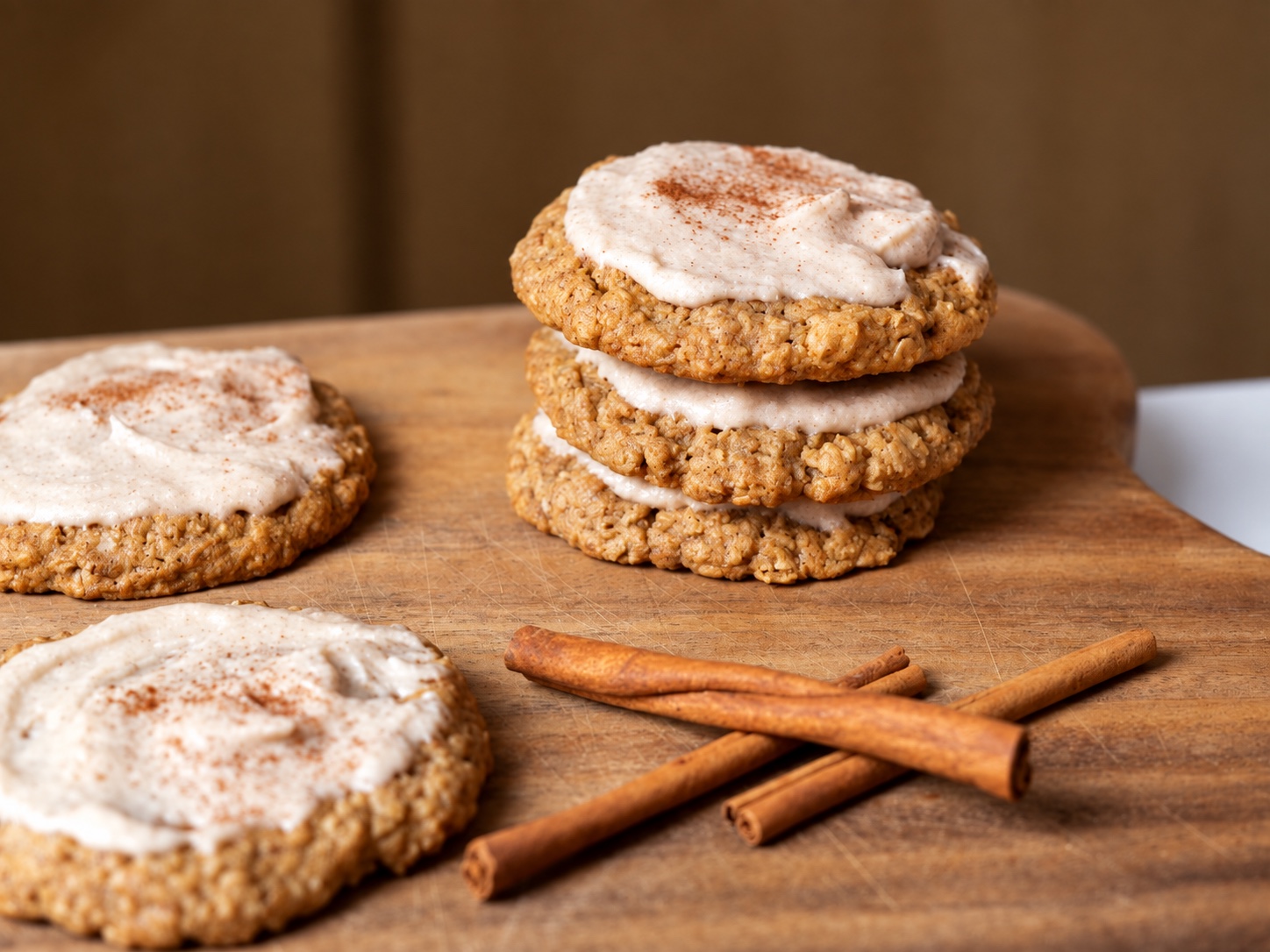 Frosted apple butter oatmeal cookies stacked on a wooden board with cinnamon sticks.
