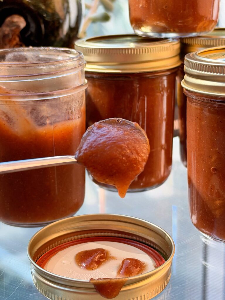 Thick homemade apple butter dripping slowly from a spoon in front of filled jars.