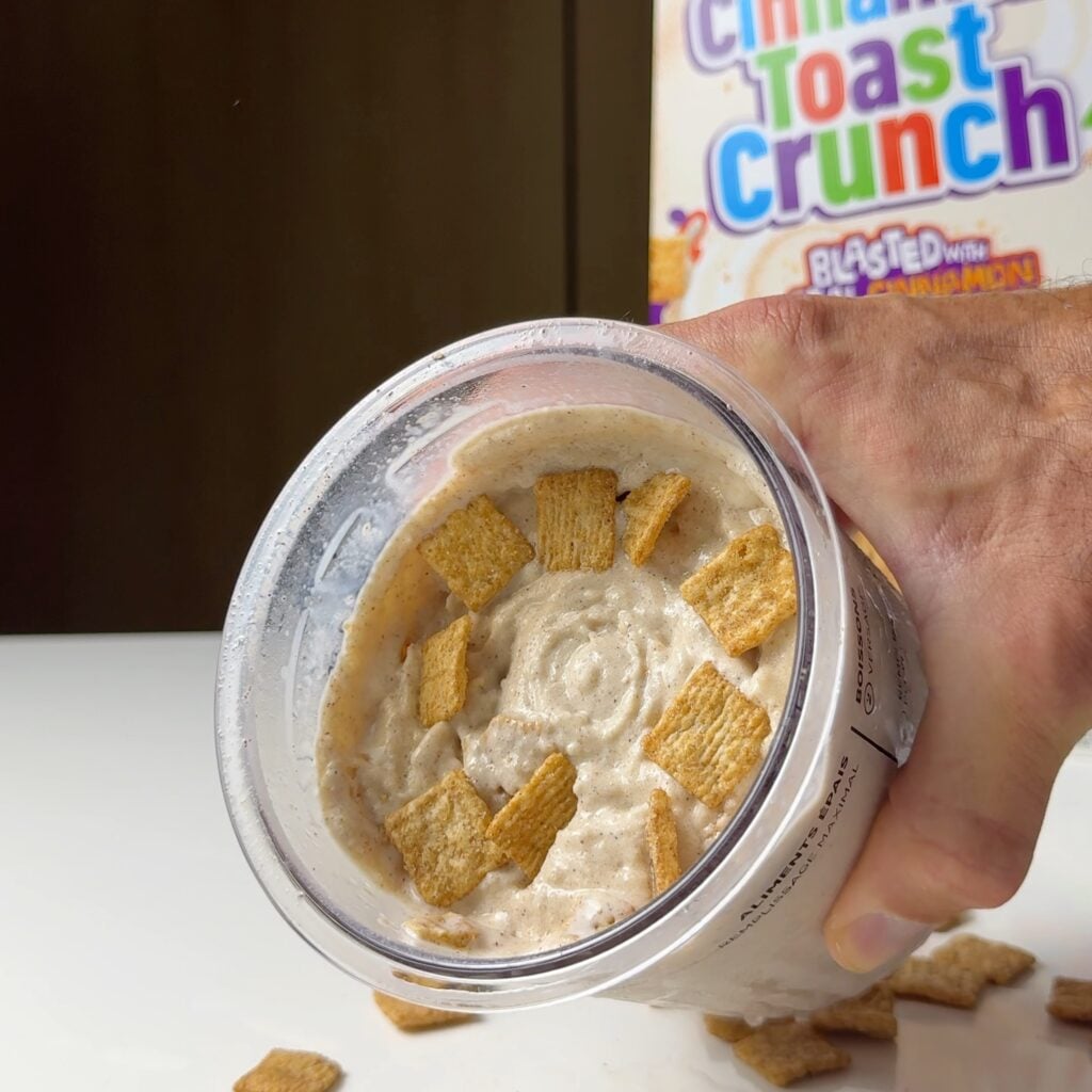 Top view of a hand holding high-protein Cinnamon Toast Crunch Ninja Creami topped with cereal pieces.