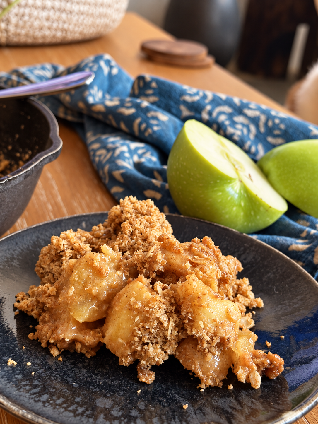 Close-up serving of warm gluten-free apple crisp with tender apples and golden oat topping on a dark plate.