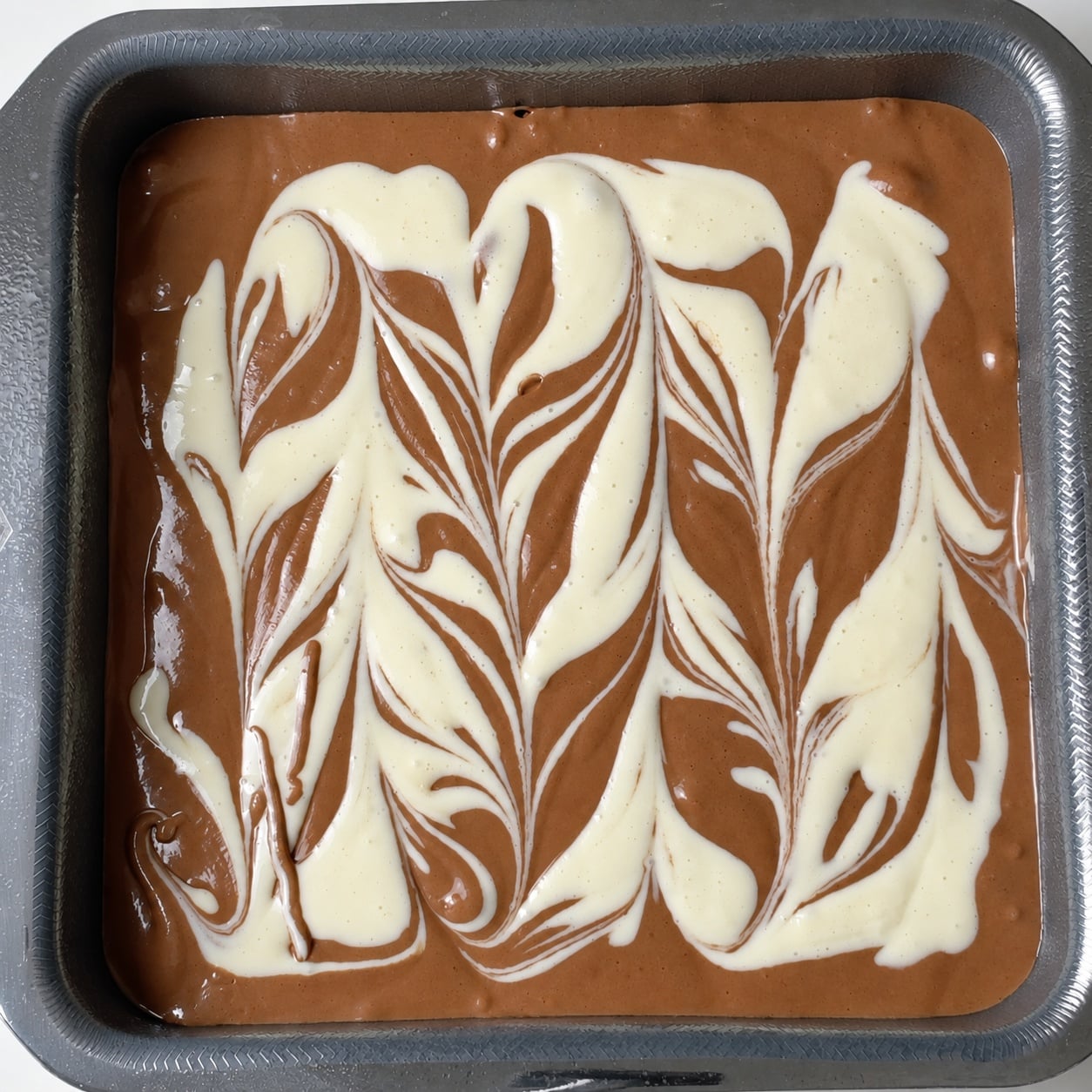 Unbaked chocolate brownie batter with cream cheese swirl in a square pan