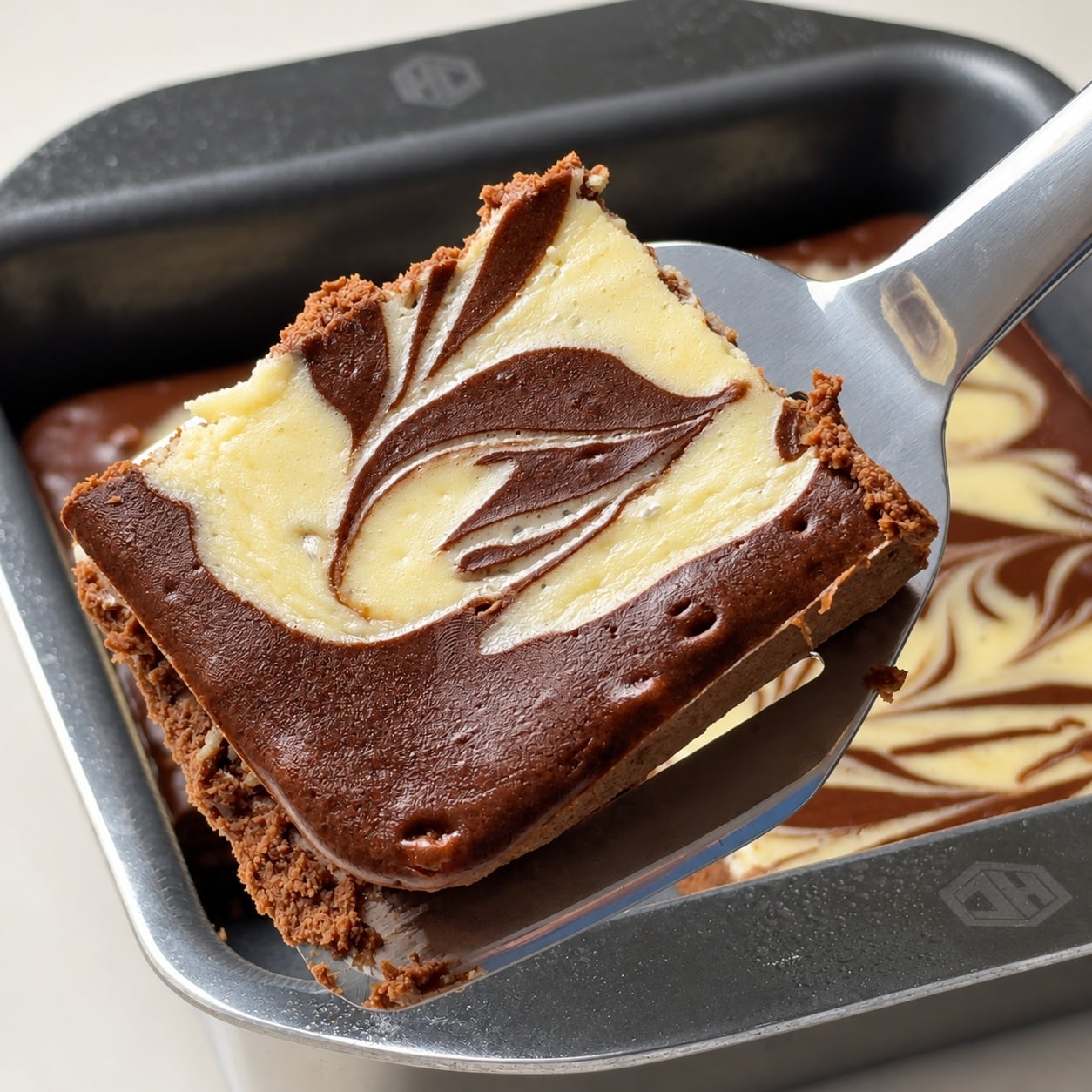 High-protein cheesecake brownie square lifted from the baking pan