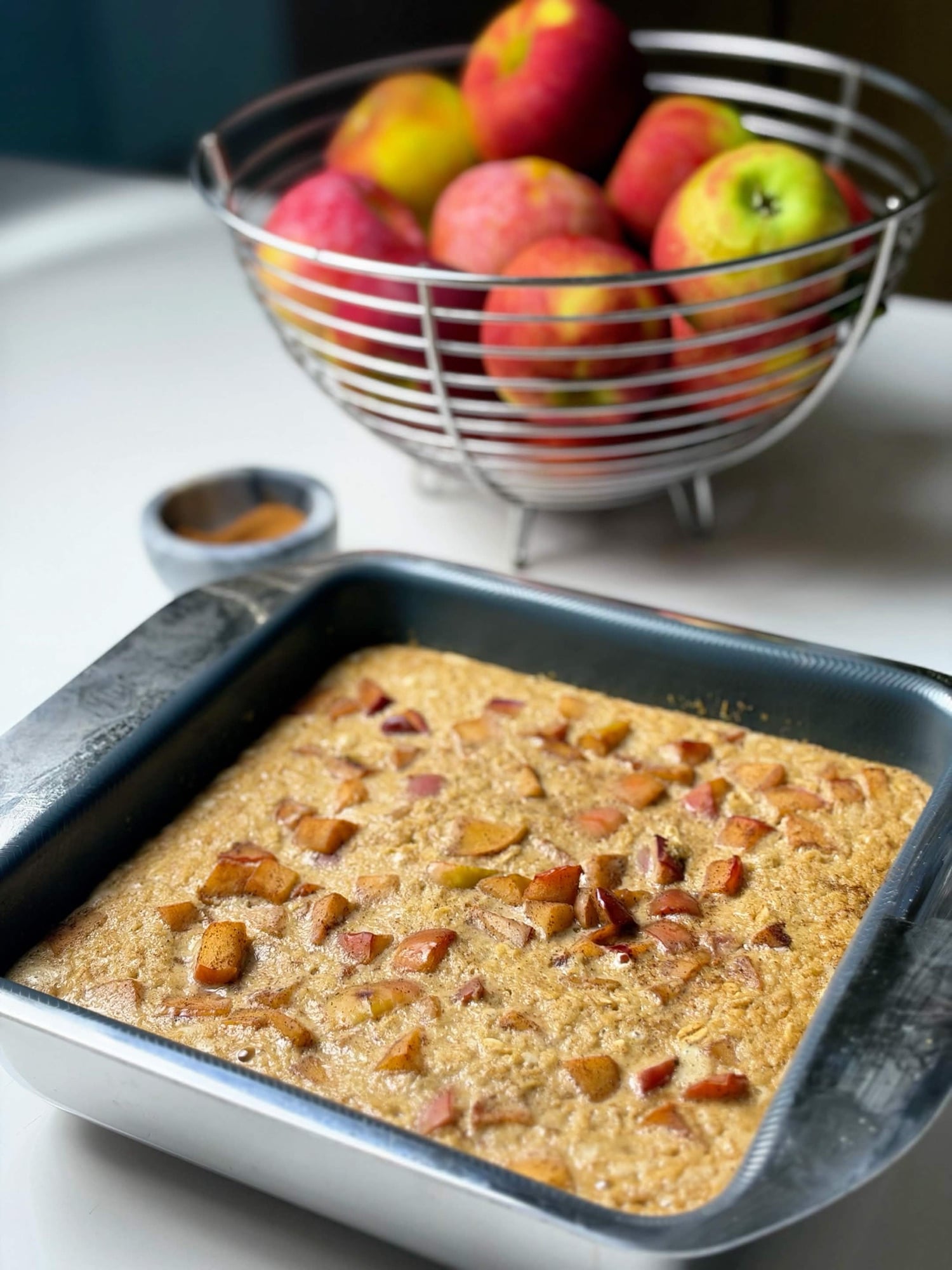 High-protein apple pie baked oatmeal in a square pan with fresh apples in the background